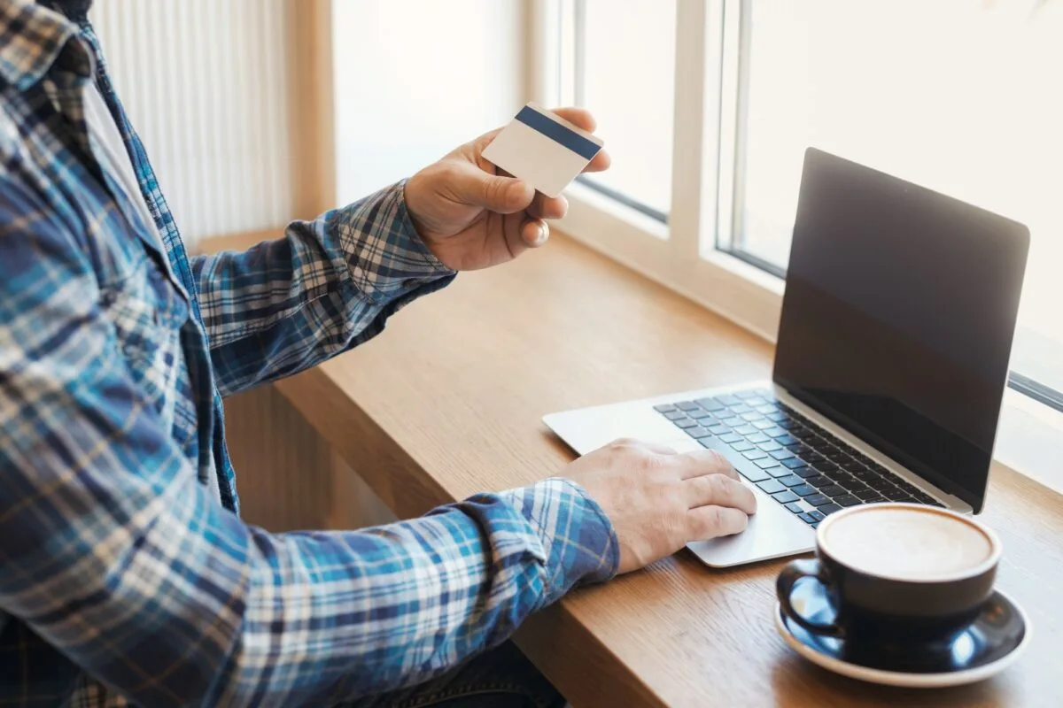 Homme tenant une carte bancaire et utilisant un ordinateur portable